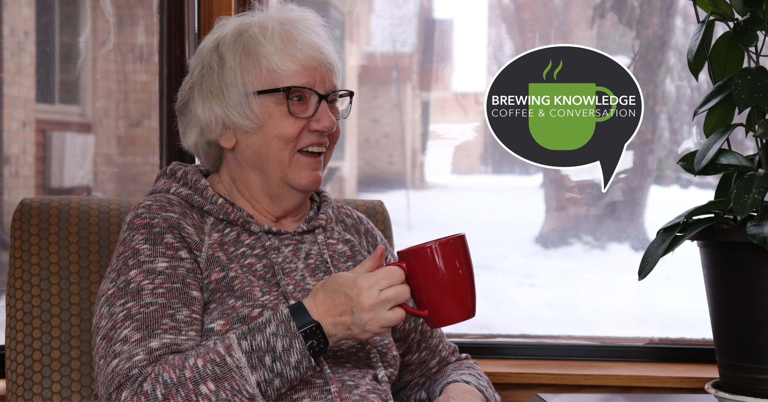 Elderly person with glasses smiles while holding a red mug indoors. Snowy view outside. Logo beside them reads "Brewing Knowledge Coffee and Conversation."